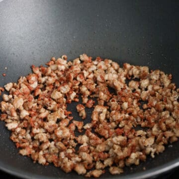 Ground pork browning and becoming crispy in a large hot skillet.