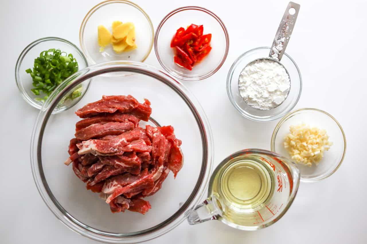 Separate bowls of sliced flank steak, red chili, green onions, garlic, ginger, vegetable oil, and cornstarch to make mongolian beef.