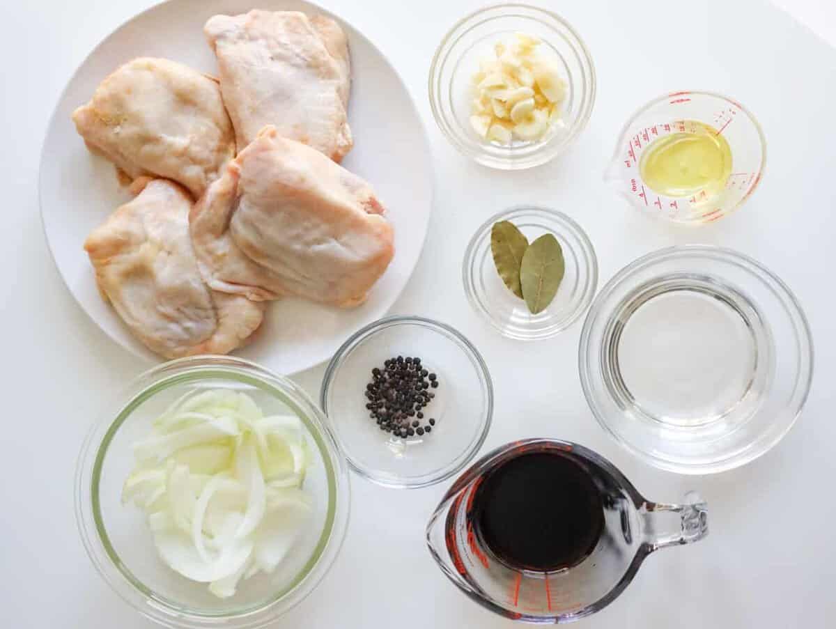 Ingredients for chicken adobo including chicken thighs, onion, soy sauce, rice vinegar, garlic, peppercorns, and bay leaves.