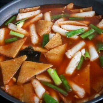 Rice cakes, fish cakes, and green onions simmering in sauce.