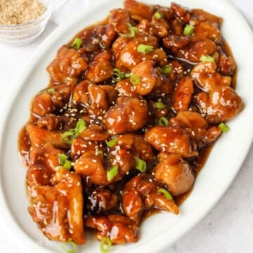 Crispy fried chicken pieces tossed and coated in glossy honey sesame sauce, garnished with sliced green onions and sesame seeds in a pan.