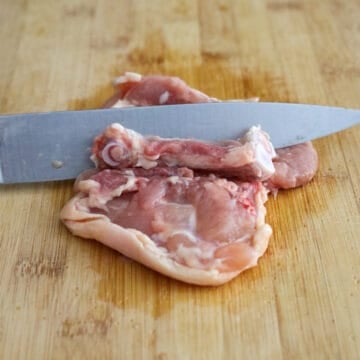 Raw skin-on chicken thigh being deboned.