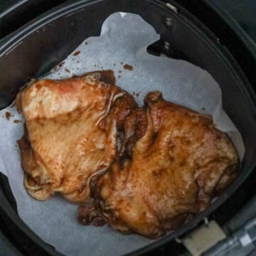 Marinated chicken thighs arranged in the air fryer basket skin-side up in a single layer.