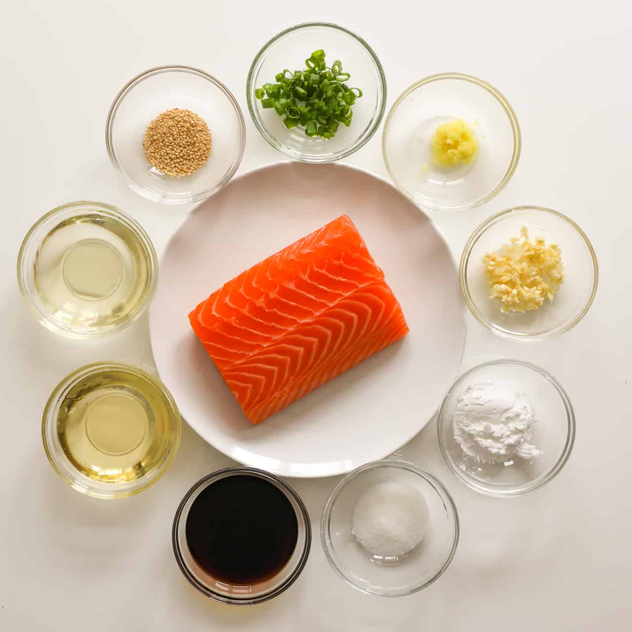 Ingredients for air fryer teriyaki salmon, including salmon, soy sauce, sake, mirin, sugar, cornstarch, garlic, ginger, green onion, and sesame seeds