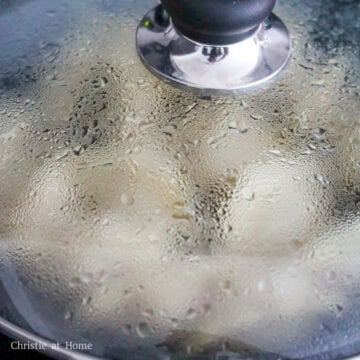 Pork dumplings cooking in a shallow layer of bubbling water.
