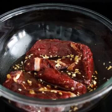 Steaks coated in marinade in a large bowl.
