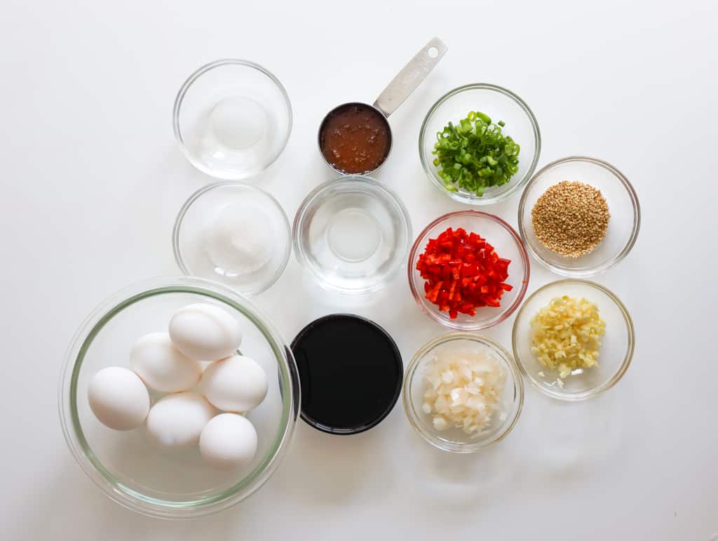 Mayak eggs ingredients including eggs, soy sauce, honey, onion, Korean red chili pepper, green onion, garlic, and sesame seeds.