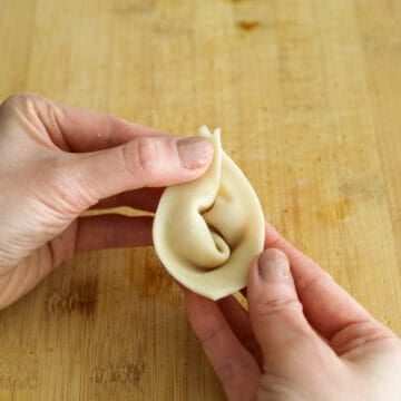 Then bring the two pointed ends of the wings together and pinch to seal them. Repeat this process for remaining wontons.