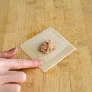 Prepare a small bowl of water nearby. On a clean working surface, lay out one wonton skin flat. Add 1 teaspoon of filling into the center of each wrapper. Using your finger or the back of the spoon, dab water along the corner of a wonton wrapper.