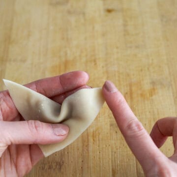 Fold the wonton into a triangle so the opposite corner is sealed to the other one. Push out any air bubbles and seal the edges of the wrapper. With your triangle, lightly dab water on the end of one wing.