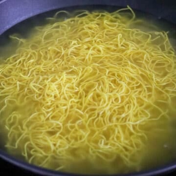 Yellow wheat noodles loosening in clear bubbling water.