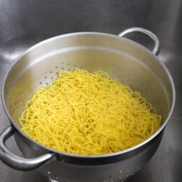 Steam rising from yellow wheat noodles straining inside a colander.