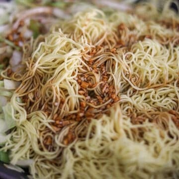 Yellow wheat noodles and a dark brown glaze settling next to cooked vegetables.