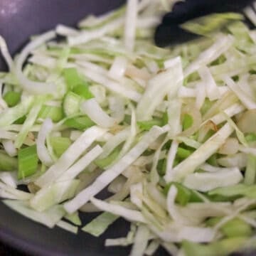 Shredded green cabbage, celery angles, and sliced white onions cooking down together.
