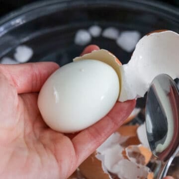 Cracked eggshell being peeled from a soft-boiled egg.