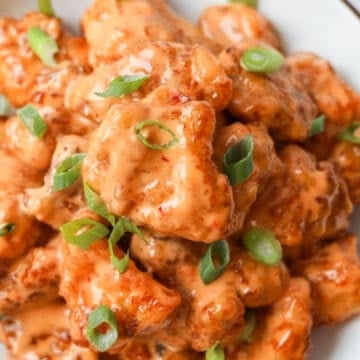 Crispy fried chicken pieces coated in glossy pink sauce are garnished with green onions.