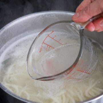 Long noodles boiling in a pot of hot water on the stovetop.