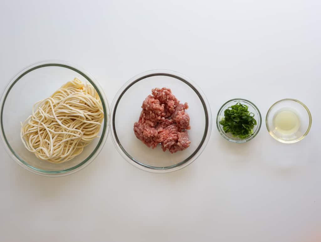 Thick wheat noodles, ground meat, green onions, and oil on a table.
