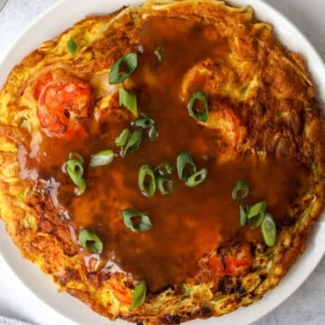 Egg foo young covered in glossy brown gravy and garnished with chopped green onions.