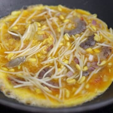 Egg mixture with shrimp, bean sprouts, and shallots spread evenly for frying.