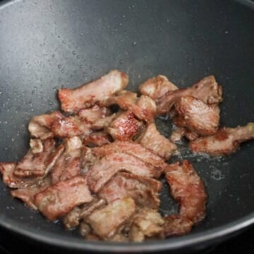 Sliced flank steak searing with browned edges in oil.