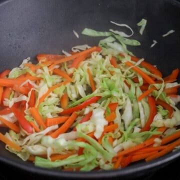 Sliced orange carrots, red bell peppers, and shredded green cabbage cooking together.