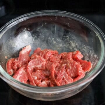 Sliced raw beef marinating in a bowl with soy sauce and cornstarch.