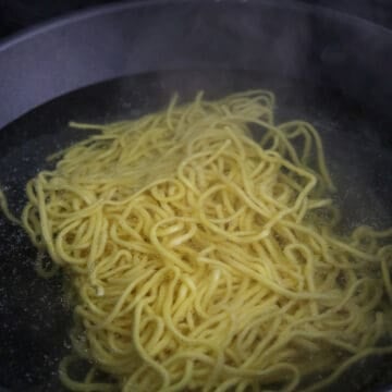 Thick yellow egg noodles blanching in hot boiling water in a pan.