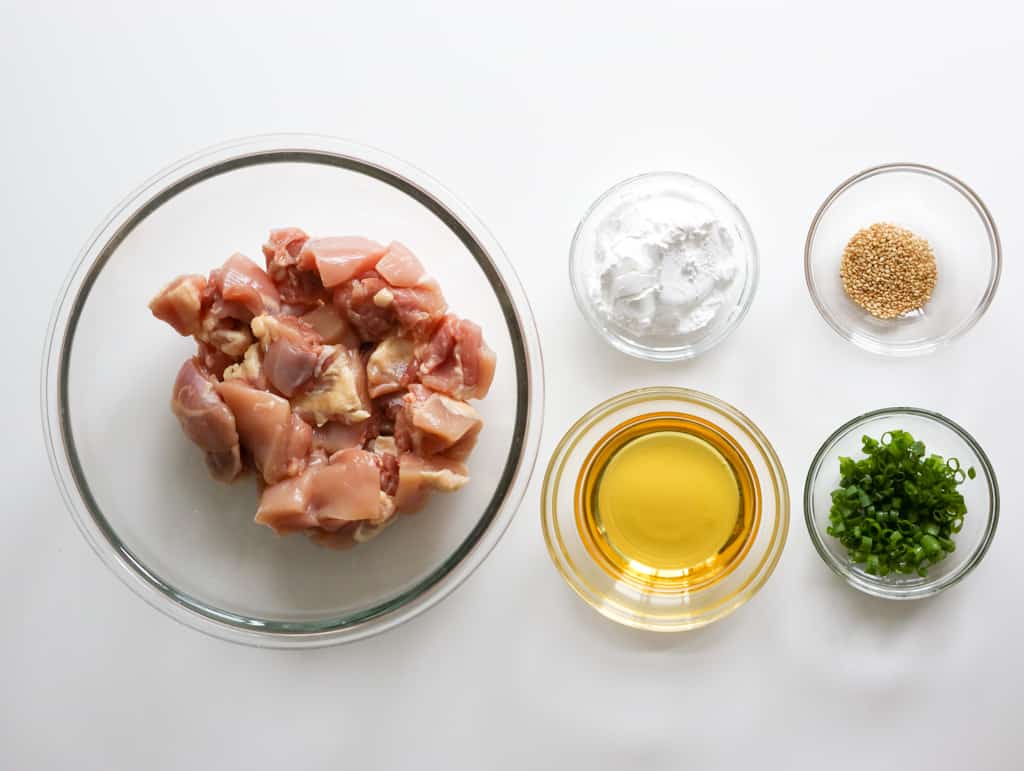 Cubed chicken thighs, vegetable oil, green onions, and toasted sesame seeds for crispy ginger chicken.