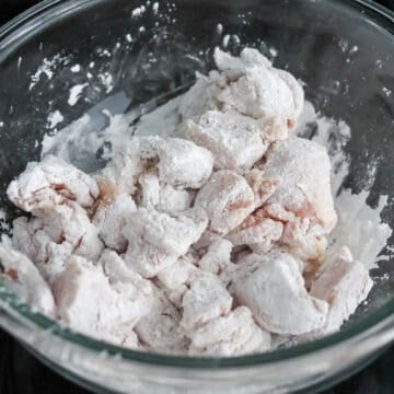 Chicken pieces being tossed in cornstarch, evenly coating each piece in a light, powdery layer.