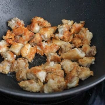 Chicken frying in a pan of hot oil, turning golden brown and crispy as it cooks in small batches.