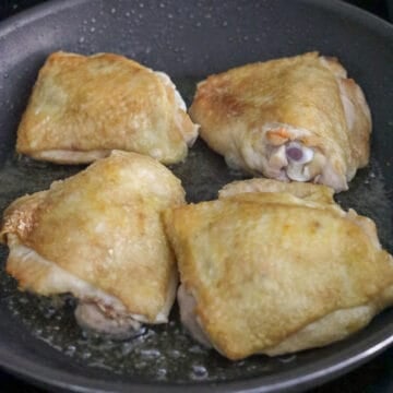 Raw chicken thighs searing skin-side down in a hot, glistening pan.
