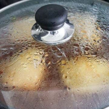Dark brown soy sauce glaze simmering around chicken thighs under a lid.