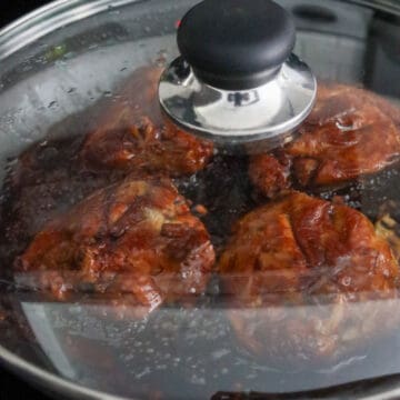 Simmering chicken thighs being flipped over in a dark brown sauce.