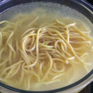 Fresh lo mein noodles soaking in boiling water until loosened.