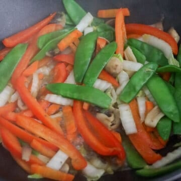 Sliced carrots, bell pepper, snow peas, mushrooms, and napa cabbage stir-frying together.