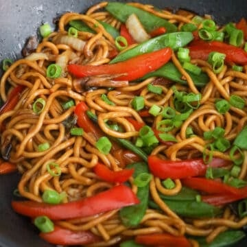 Lo mein noodles and vegetables coated in glossy sauce with green onions and sesame seeds.