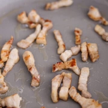 Sliced pork belly cooking in a pan until the edges are golden and the fat has rendered.