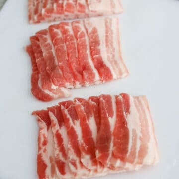 Raw strips of thinly sliced pork belly cut into uniform pieces.
