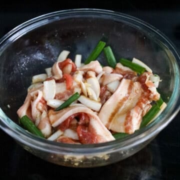 Sliced pork belly coated thoroughly with savory brown marinade and mixed with chopped aromatics.