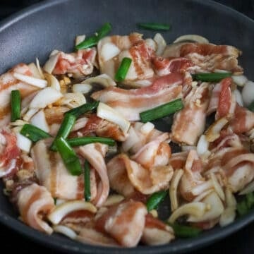 Searing pork belly slices glistening with liquids and aromatics over heat.