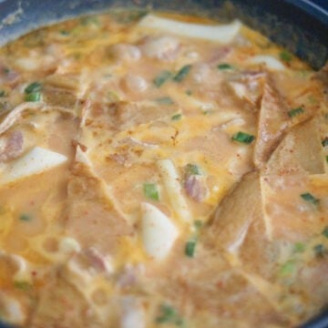 Rosé tteokbokki simmering in a pan with fish cakes and rice cakes in a thick, creamy sauce.