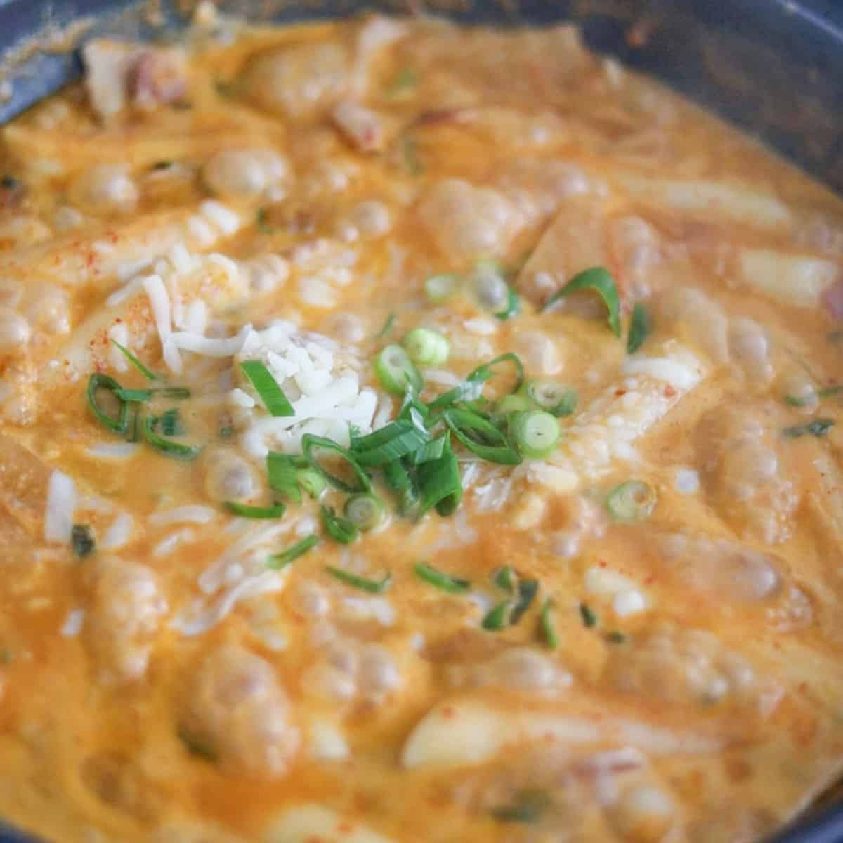 Finished rosé tteokbokki topped with melted cheese and green onions, ready to serve.