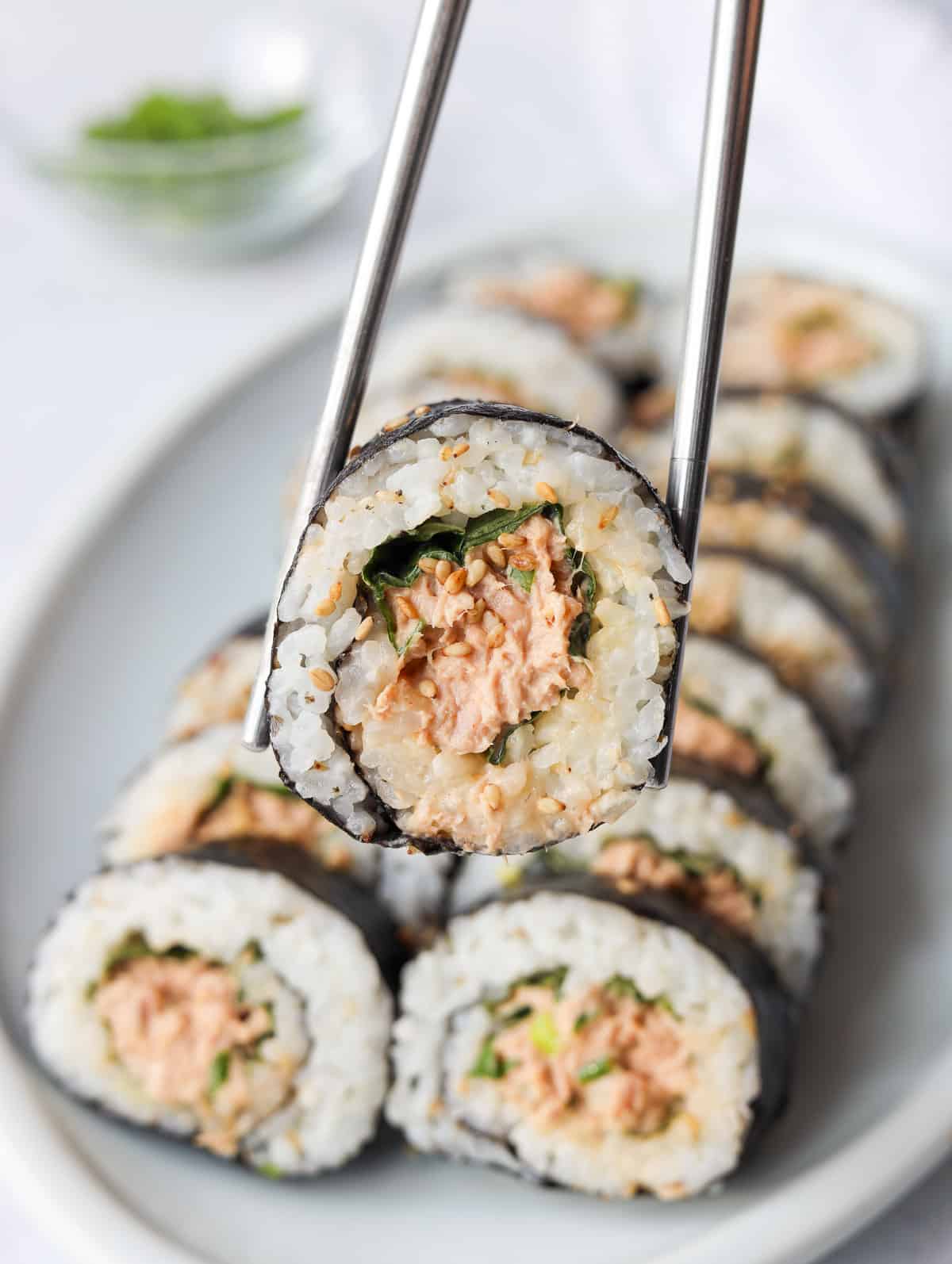 a slice of spicy tuna kimbap being held by chopsticks