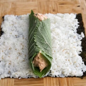 Perilla leaves layered over seasoned rice with spicy tuna shaped into a thick log.