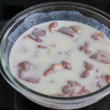 White liquid buttermilk is poured over raw cubed chicken to marinate.