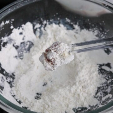Chicken pieces are tossed in dry cornstarch seasoning mixture until coated.
