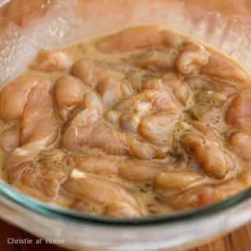 Sliced chicken breast in a mixing bowl being coated evenly with marinade ingredients.
