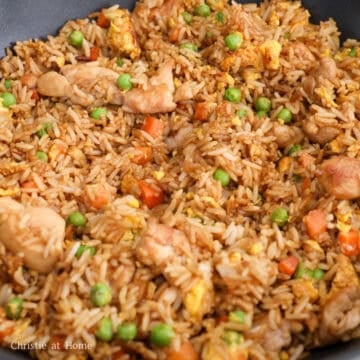Chicken fried rice evenly coated in savory sauce with chicken, eggs, peas, and carrots.