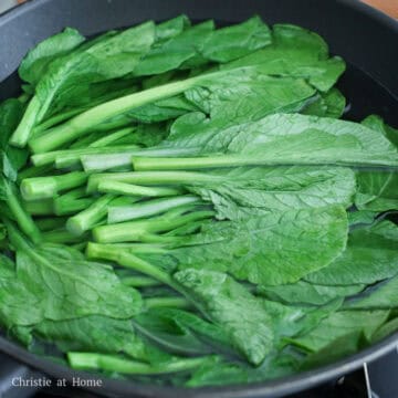Yu choy blanching in a large pot of boiling water.